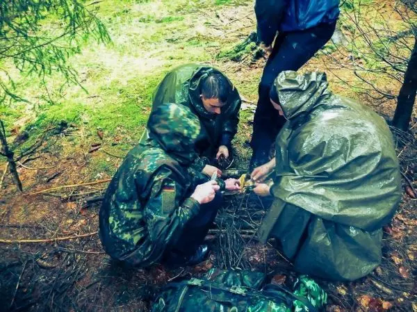 Drei Personen sammeln Äste und bereiten ein Feuer im Wald vor