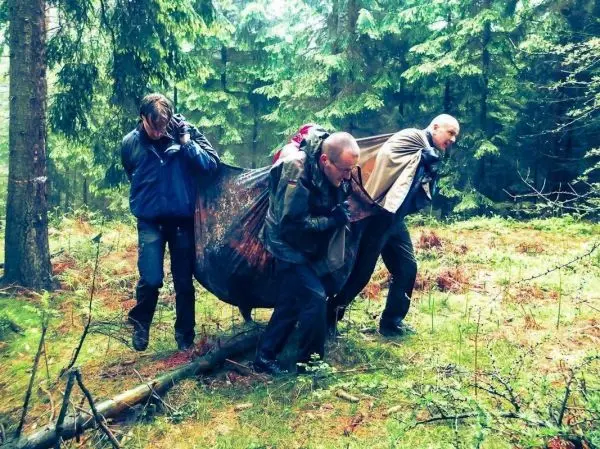 Drei Personen tragen eine improvisierte Trage durch den Wald