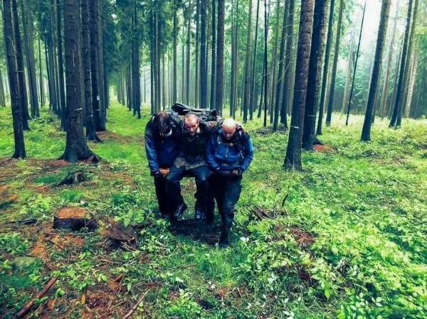 Drei Personen tragen einen verletzten Wanderer durch einen Waldweg