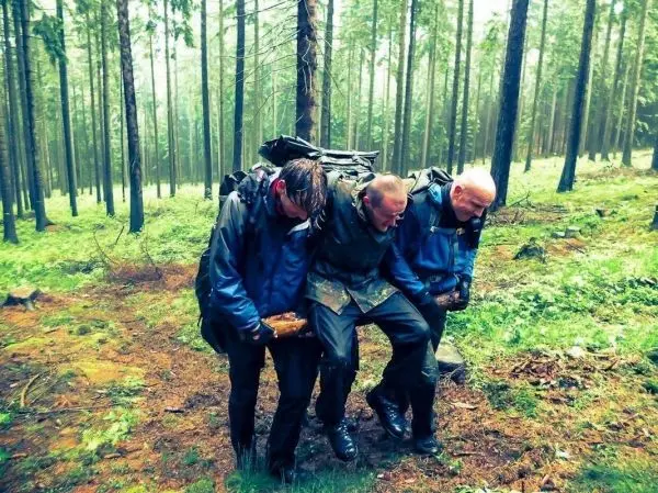 Drei Personen tragen gemeinsam eine improvisierte Trage durch den Wald