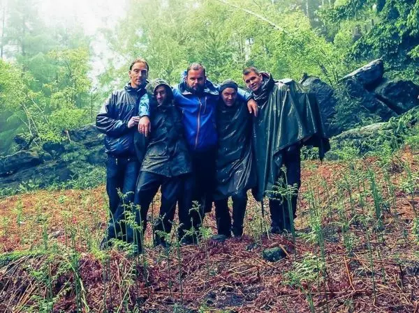 Fünf Personen in Regenjacken stehen in einem bewaldeten Gebiet mit feuchtem Boden