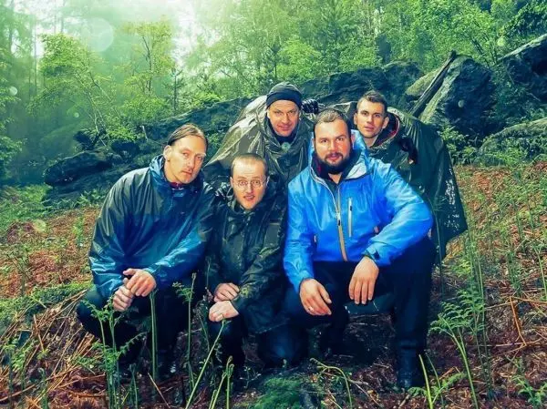 Gruppierung von fünf Personen in Regenjacken, umgeben von Wald und Felsen