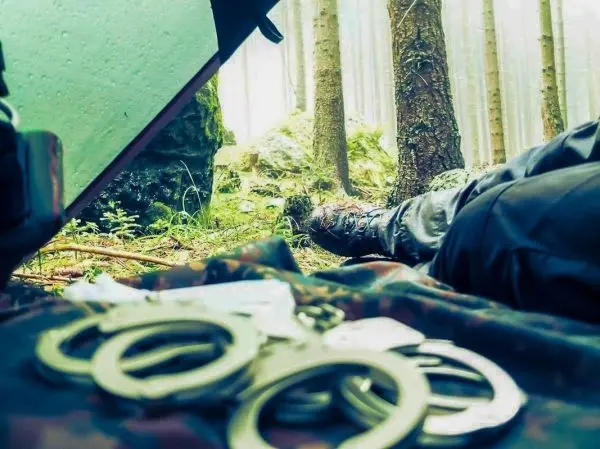 Handschellen liegen auf einem Tuch im Wald, im Hintergrund ein Fuß in Stiefel