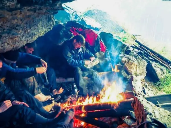 Kleines Bodenfeuer in einer Höhle, mehrere Personen sitzen um das Feuer