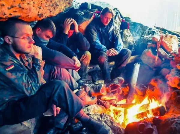 Kleines Bodenfeuer in einer Höhle, vier Personen sitzen um das Feuer