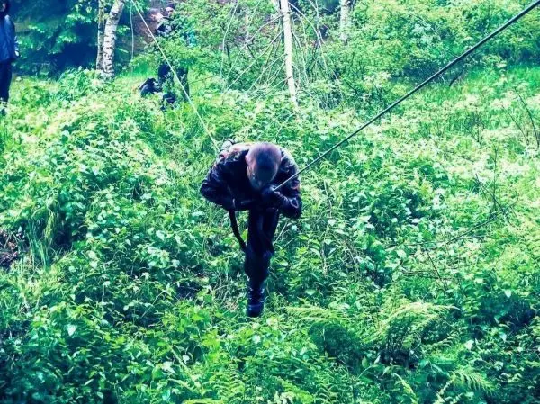 Mann überquert eine selbstgebaute Seilbrücke in dichtem Grün