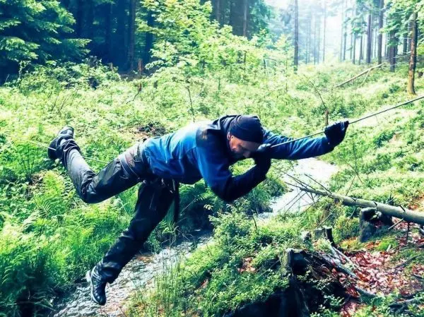 Mann überquert einen kleinen Bach mit einer selbstgebauten Seilquerung