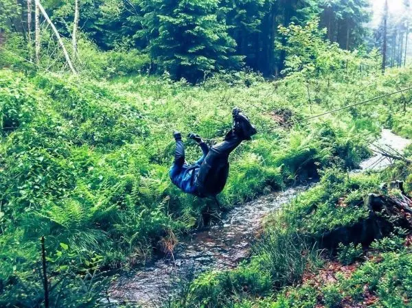Person hängt kopfüber an einem Seil über einem Bach im Wald