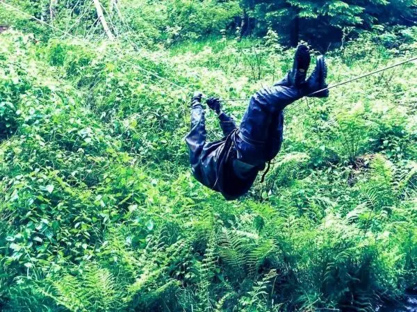 Person hängt kopfüber an einem Seil zwischen Bäumen