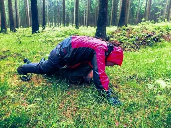 Person in roter Jacke führt eine Low Crawl-Technik im Wald aus