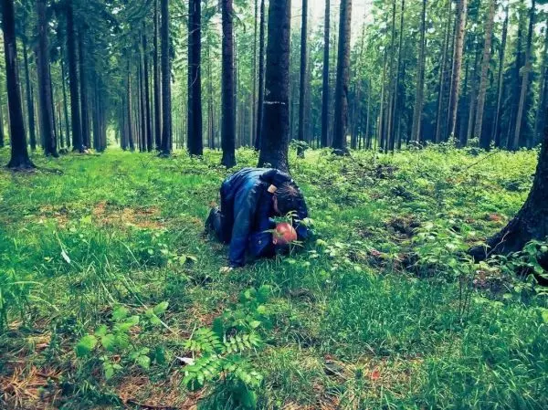 Person kniet im Gras zwischen Bäumen und schaut nach unten