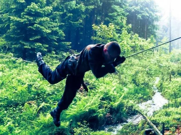 Person schwingt an einem Seil über eine bewachsene Fläche