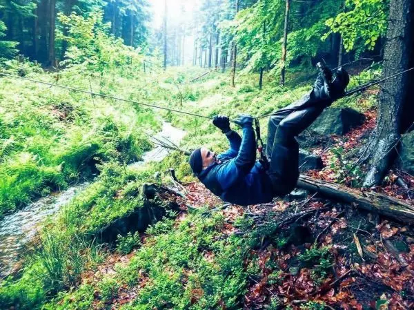 Person schwingt an einem Seil über einen Bach im Wald