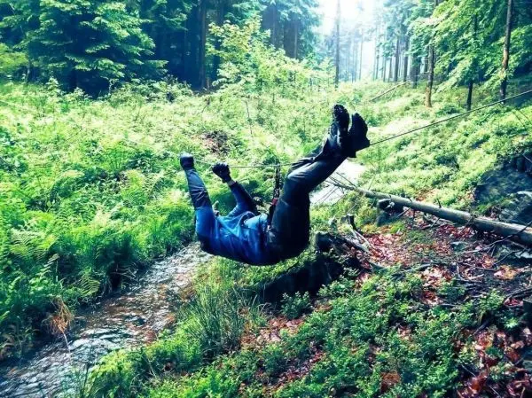 Person schwingt an einem Seil über einen Bach im Wald