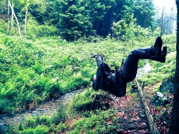 Person schwingt an Seil über einen kleinen Bach im Wald