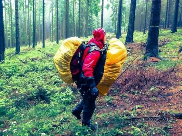 Person trägt zwei gelbe Packsäcke im Wald