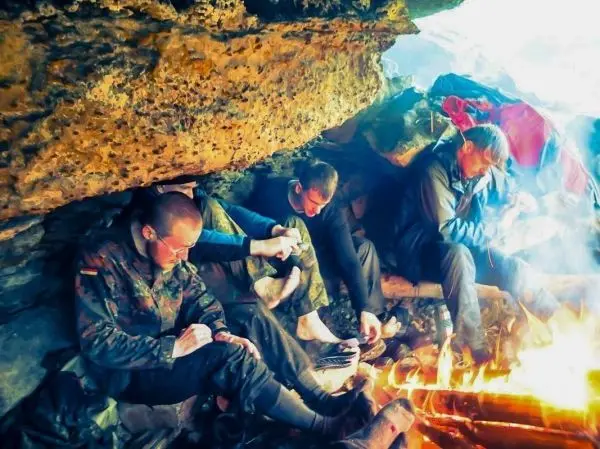 Personen sitzen unter einem Felsen und wärmen sich am Feuer