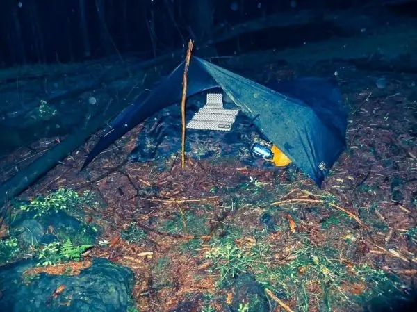 Tarp-Notunterkunft aus einem Tarp und Ästen auf dem Boden