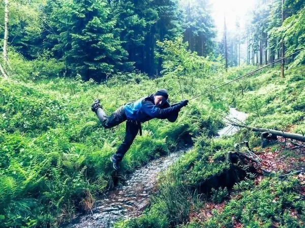 Überquert eine selbstgebaute Seilbrücke über einen kleinen Bach im Wald