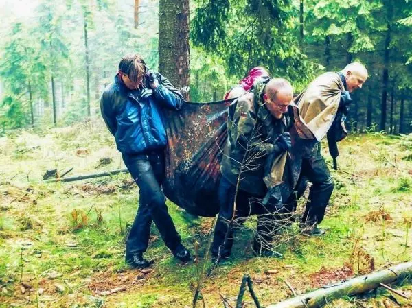 Vier Personen tragen eine improvisierte Trage durch den Wald