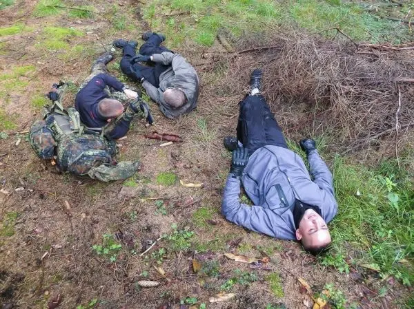 Drei Personen liegen auf dem Boden in einem Waldgebiet