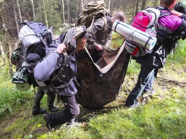 Drei Personen tragen eine improvisierte Trage durch den Wald