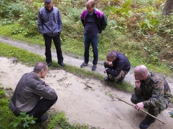 Fünf Personen betrachten Spuren im Sand auf einem Waldweg