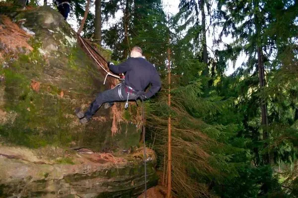 Kletterer sichert sich mit Seil an einer Felswand im Wald