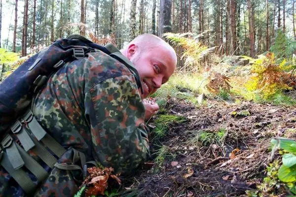 Mann in Tarnkleidung liegt am Boden und beobachtet den Waldboden