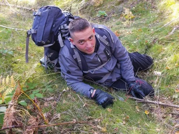 Mann liegt auf dem Boden und bearbeitet einen Stock im Unterholz