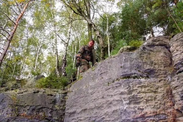 Mann mit Ausrüstung steht auf einem Felsen in bewaldeter Umgebung