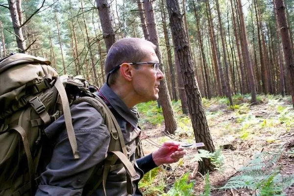 Mann mit Rucksack hält Kompass in der Hand und schaut konzentriert in den Wald