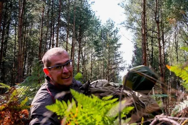 Mann trägt eine große Tasche durch einen Wald mit Bäumen und Farnen