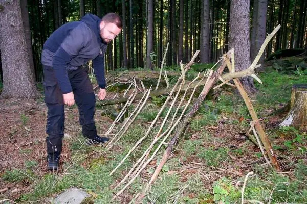 Mann überprüft eine selbstgebaute Konstruktion aus Ästen im Wald