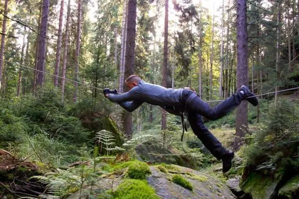 Mann überquert eine selbstgebaute Seilbrücke zwischen Bäumen im Wald