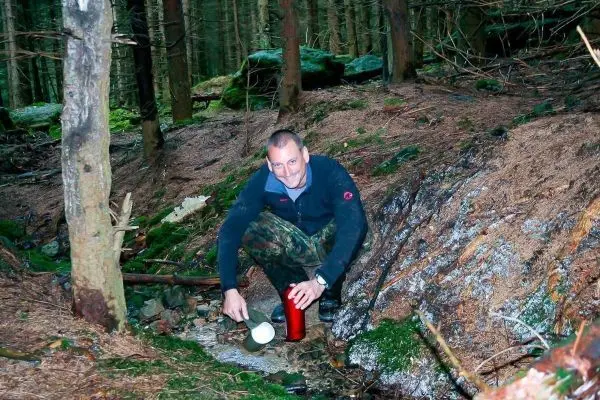 Person füllt eine Flasche aus einem kleinen Bach