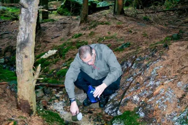 Person füllt eine Flasche mit Wasser aus einer Quelle