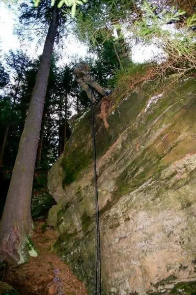Person klettert an einem Seil über einen Felsen im Wald