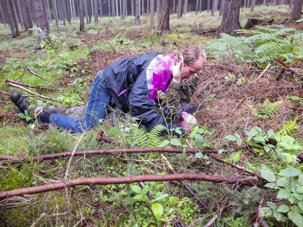 Person kniet im Wald und untersucht den Boden zwischen Pflanzen und Ästen