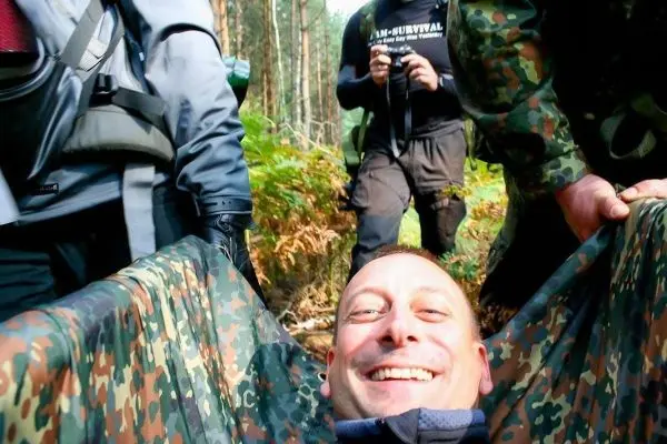 Person lächelt in einer Trage, umgeben von anderen Personen beim Überlebenstraining
