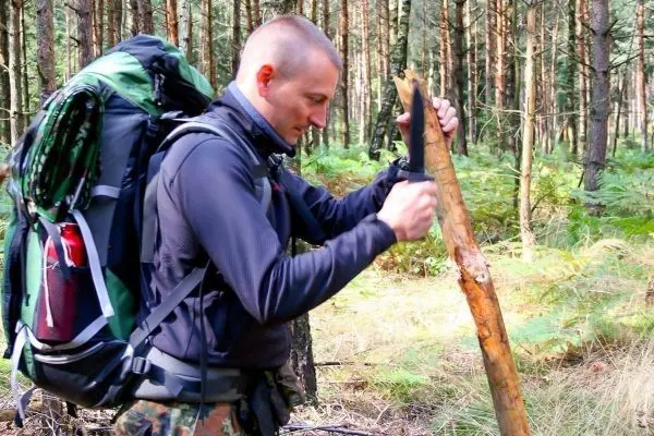 Person schnitzt mit einem Messer an einem Holzstock im Wald