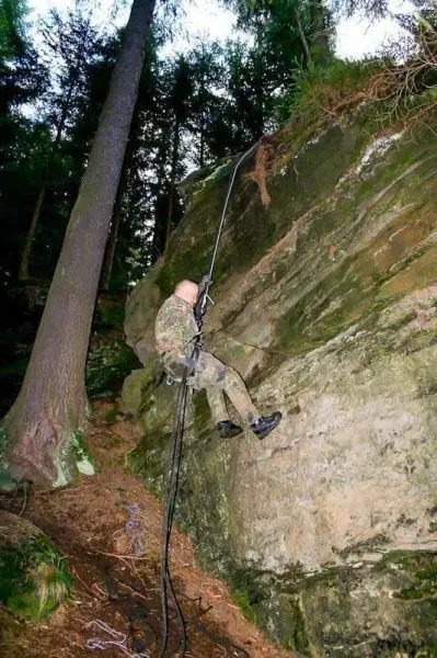 Person seilt an einer Felswand ab im Wald