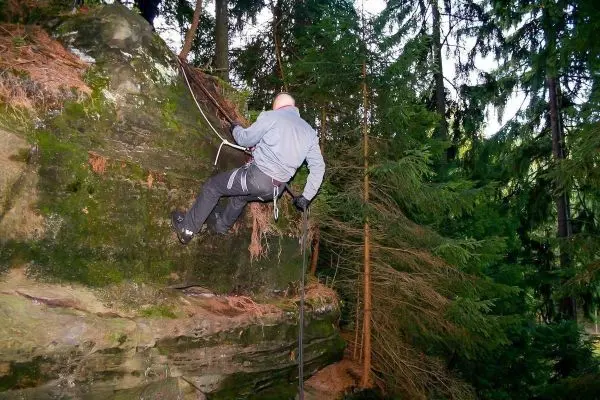 Person seilt an einer Felswand in einem Wald ab beim Überlebenstraining