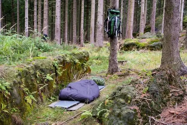 Schlafsack liegt auf einer Unterlage im Wald neben einem Rucksack