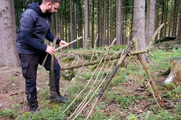 Selbstgebaute Konstruktion aus Ästen wird im Wald stabilisiert