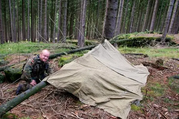 Tarp-Notunterkunft aus Plane und Ästen im Wald aufgebaut