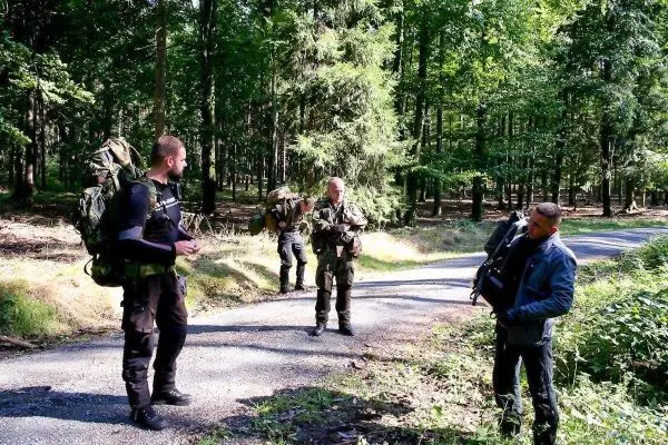 Vier Personen mit Rucksäcken stehen auf einem Waldweg und unterhalten sich