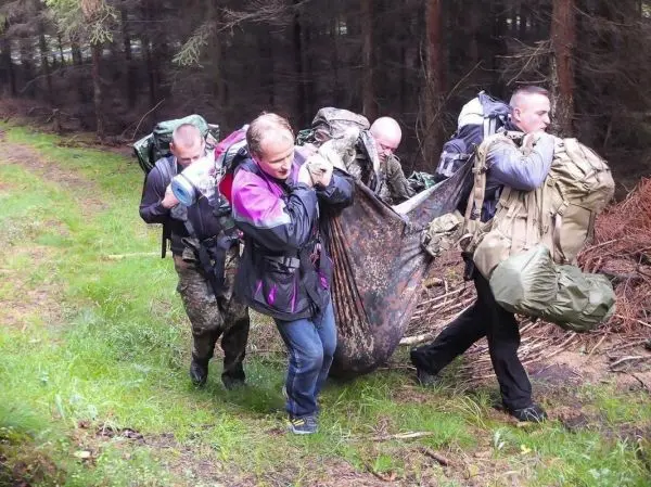 Vier Personen tragen eine improvisierte Trage durch den Wald