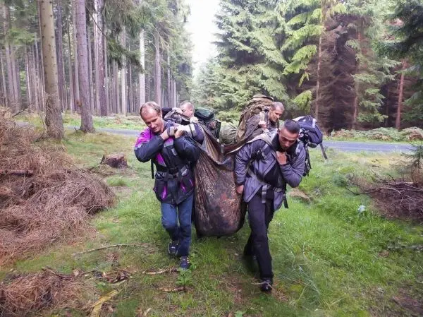 Vier Personen tragen eine improvisierte Trage durch den Wald