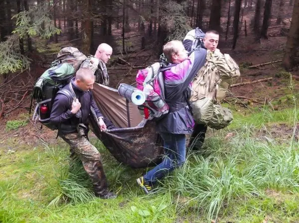Vier Personen tragen eine improvisierte Trage durch den Wald
